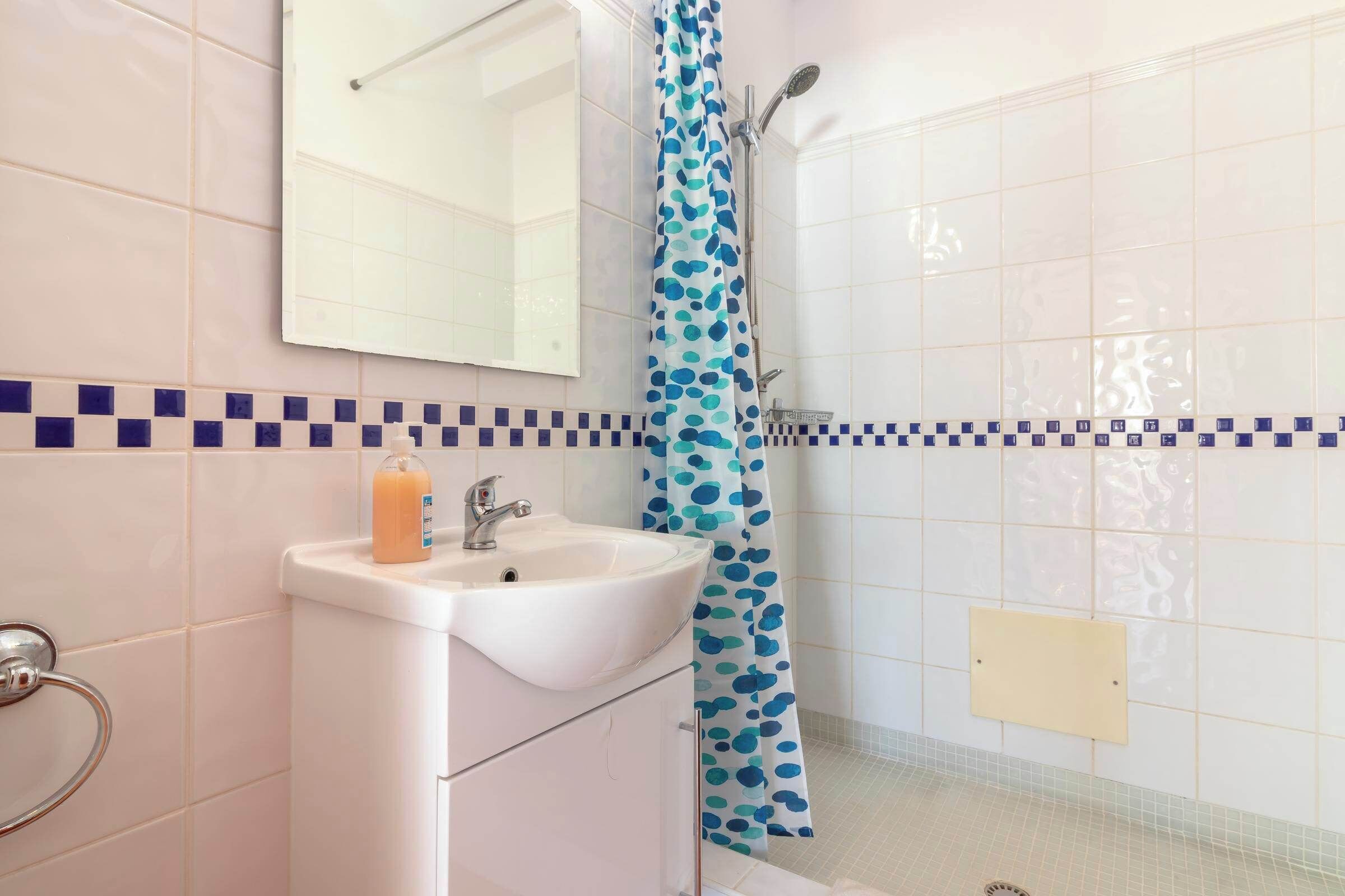 A bathroom with a sink, mirror, shower, and tiled walls.