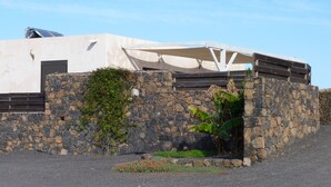 A modern building with a stone wall, a covered outdoor area, and a small garden with red flowers.