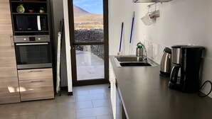 A modern kitchen with a built-in oven, microwave, and coffee maker. There is a large window with a view of a mountainous landscape.