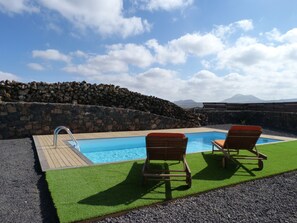 Una piscina amb dues cadires de relaxació de fusta, una paret de pedra i vistes a les muntanyes.