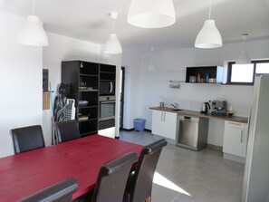 A modern kitchen with white cabinets, a red dining table, and a built-in oven.