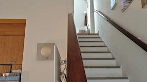 A staircase with a wooden handrail, a white wall with artwork, and a basket of fruit on the landing. - Villa with garden surrounded by greenery a stone's throw from the sea (Santa Margherita di Pula)
