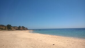 A sandy beach with clear blue water and rocky cliffs in the background.