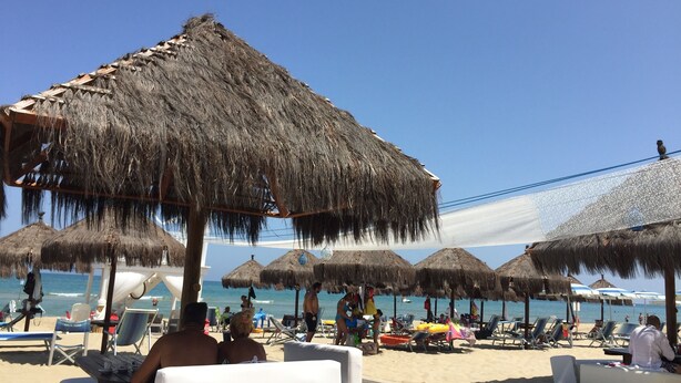 Ein Strand mit reetgedeckten Sonnenschirmen und Liegestühlen.