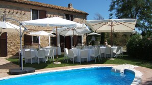 Ein Poolbereich mit Terrassentischen und Sonnenschirmen, umgeben von steinernen Gebäuden.
