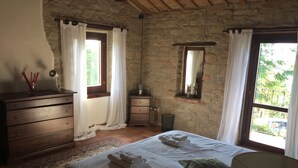 Ein Schlafzimmer mit Steinwand, Holzmöbeln, einem Bett mit Handtüchern, einem Spiegel und Blick ins Grüne.