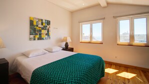 Een slaapkamer met een bed, een raam en een kunstwerk aan de muur.