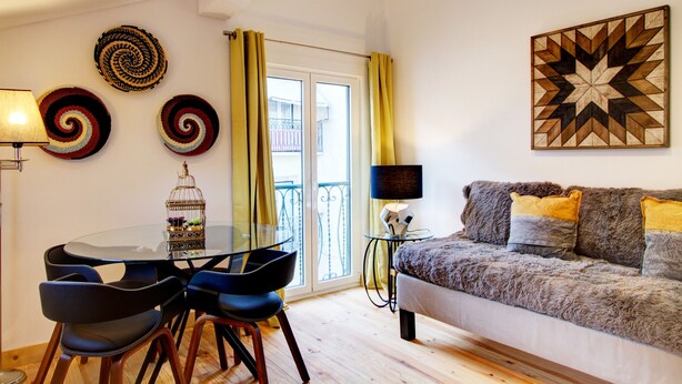 Een moderne woonkamer met een glazen tafel, zwarte stoelen, een bank met kussens, een decoratieve vogelkooi en een geometrisch kunstwerk aan de muur.