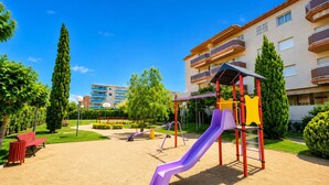 A playground with a slide and swings, surrounded by a well-maintained lawn and trees. - LOS RISCOS (La Pineda)