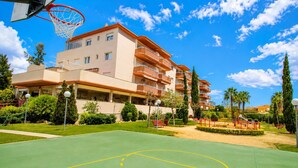 A multi-story building with balconies, a basketball court, and a clear blue sky. - LOS RISCOS (La Pineda)