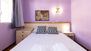 Una cama doble con dos almohadas de estampado blanco y negro, una mesita de noche con una lámpara, un cabecero de madera y un cuadro con un paisaje boscoso en la pared.