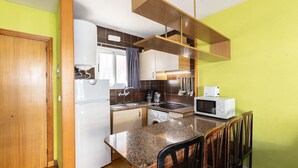Cocina compacta con refrigerador, microondas, pileta y un pequeño comedor con sillas.