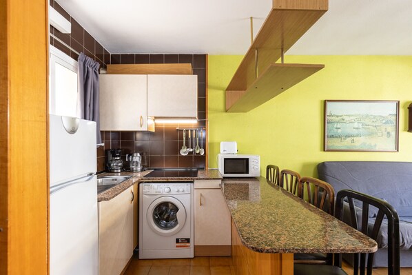 A compact kitchen with a washing machine, microwave, and a dining area with chairs.