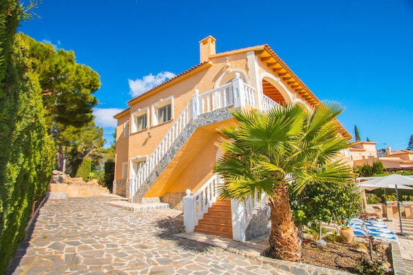 Ein Gebäude im mediterranen Stil mit einer Steintreppe, einer Palme und blauem Himmel.