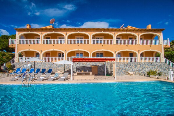 A two-story building with a swimming pool, outdoor seating, and a stone wall. - Villa Zelda - PlusHolidays (Calpe)