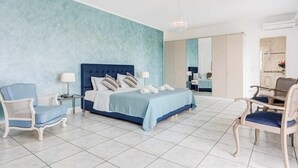 A bedroom with a bed, two chairs, a nightstand, and a mirror. - Villa Polymnia (Kefalonia)