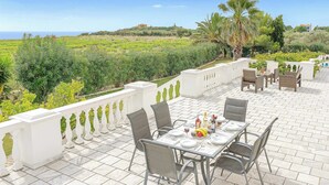 An outdoor dining area with a terrace, white balustrade, and a view of the sea and hills. - Villa Polymnia (Kefalonia)