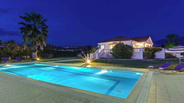 A swimming pool with lounge chairs and a house in the background. - Villa Polymnia (Kefalonia)