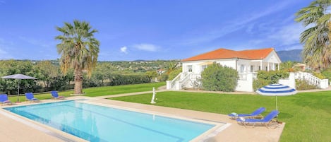 A swimming pool with lounge chairs and umbrellas, surrounded by a well-maintained lawn and palm trees.