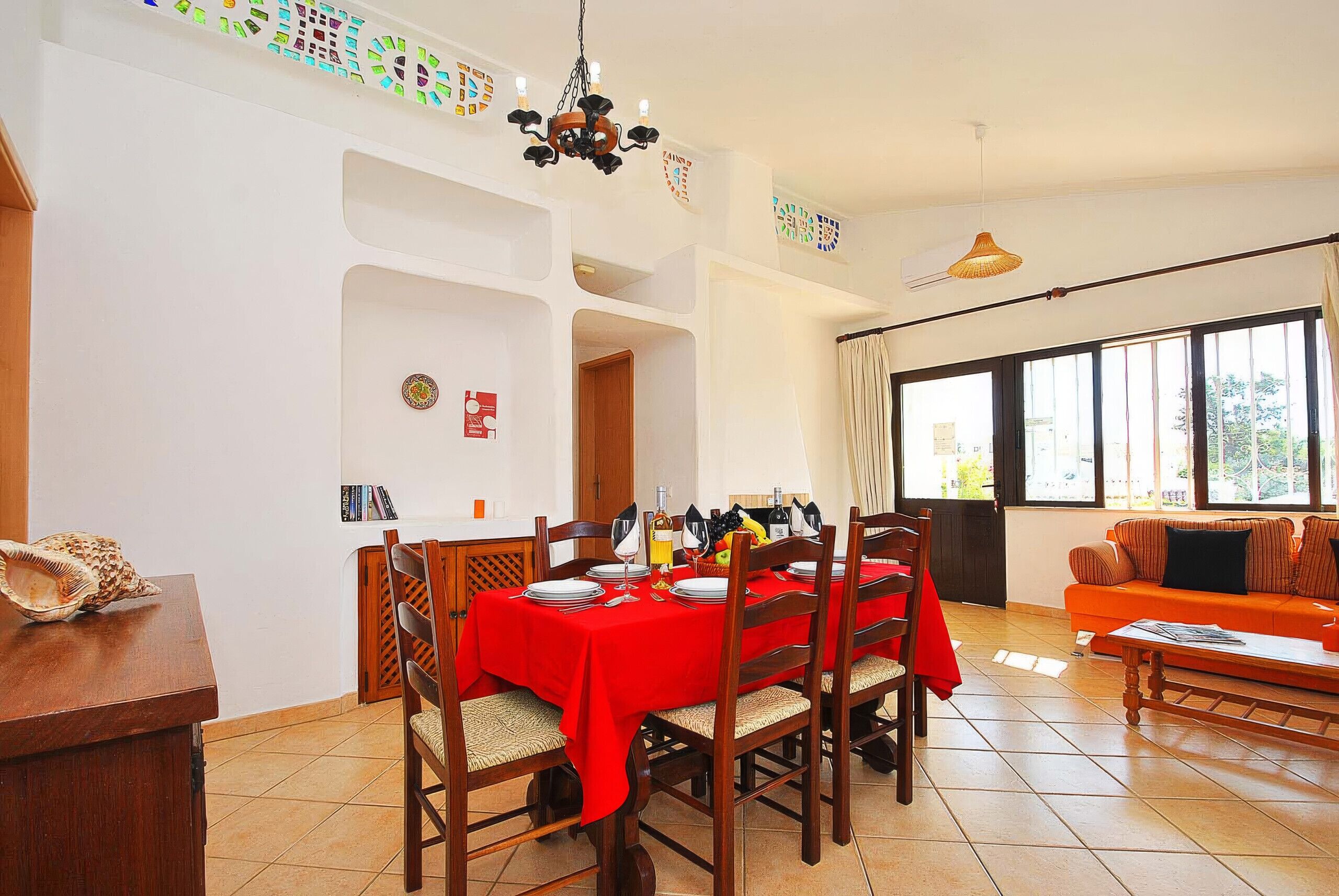 Comedor con mantel rojo, sillas de madera y una araña.