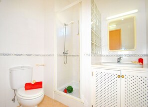 A bathroom with a toilet, shower, sink, and mirror.