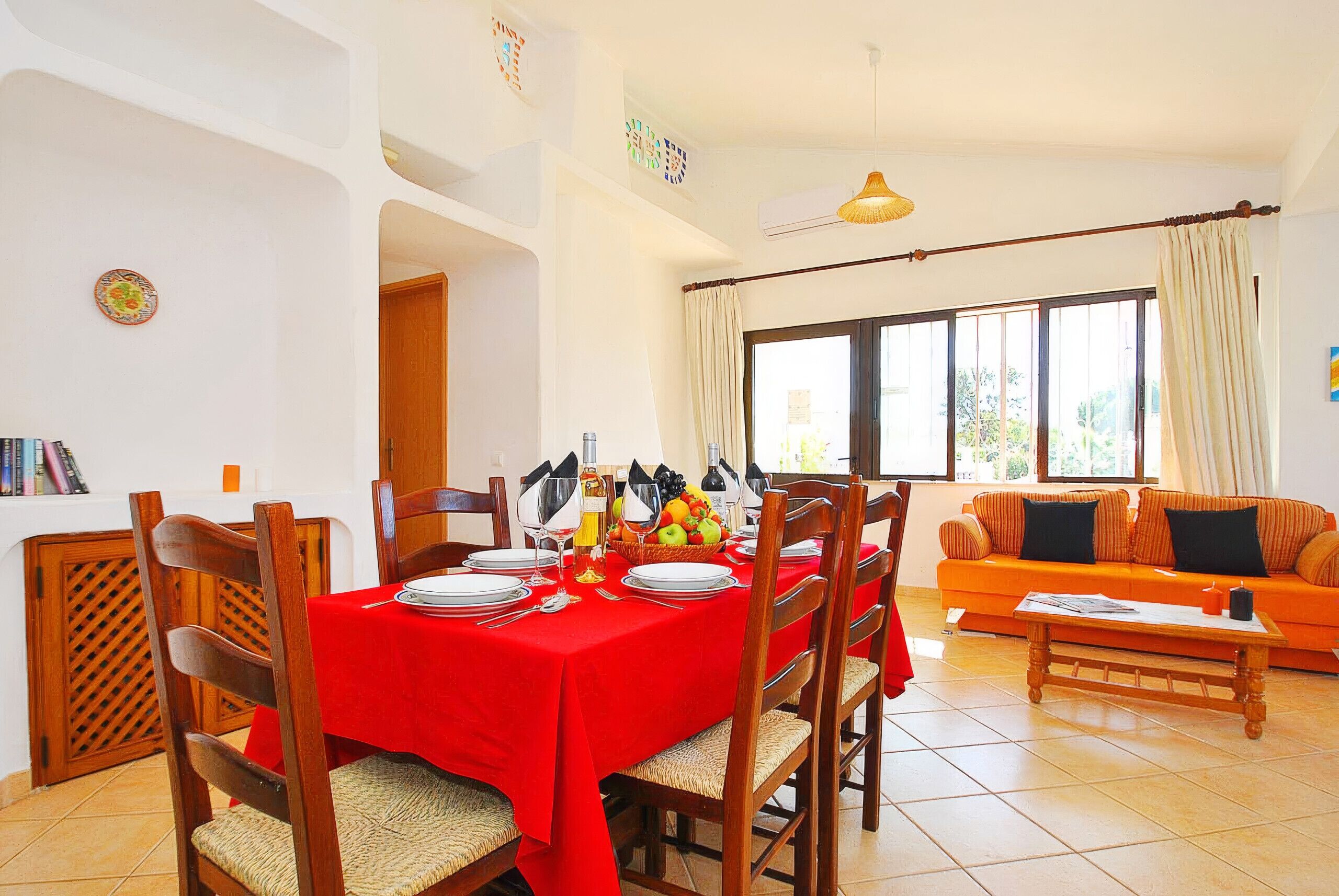 A dining area with a red tablecloth, wooden chairs, and a fruit basket.