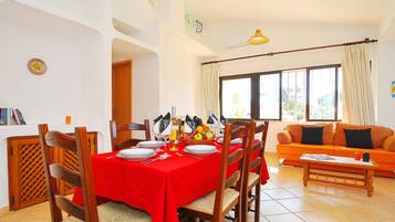 A dining area with a red tablecloth, wooden chairs, and a fruit basket.