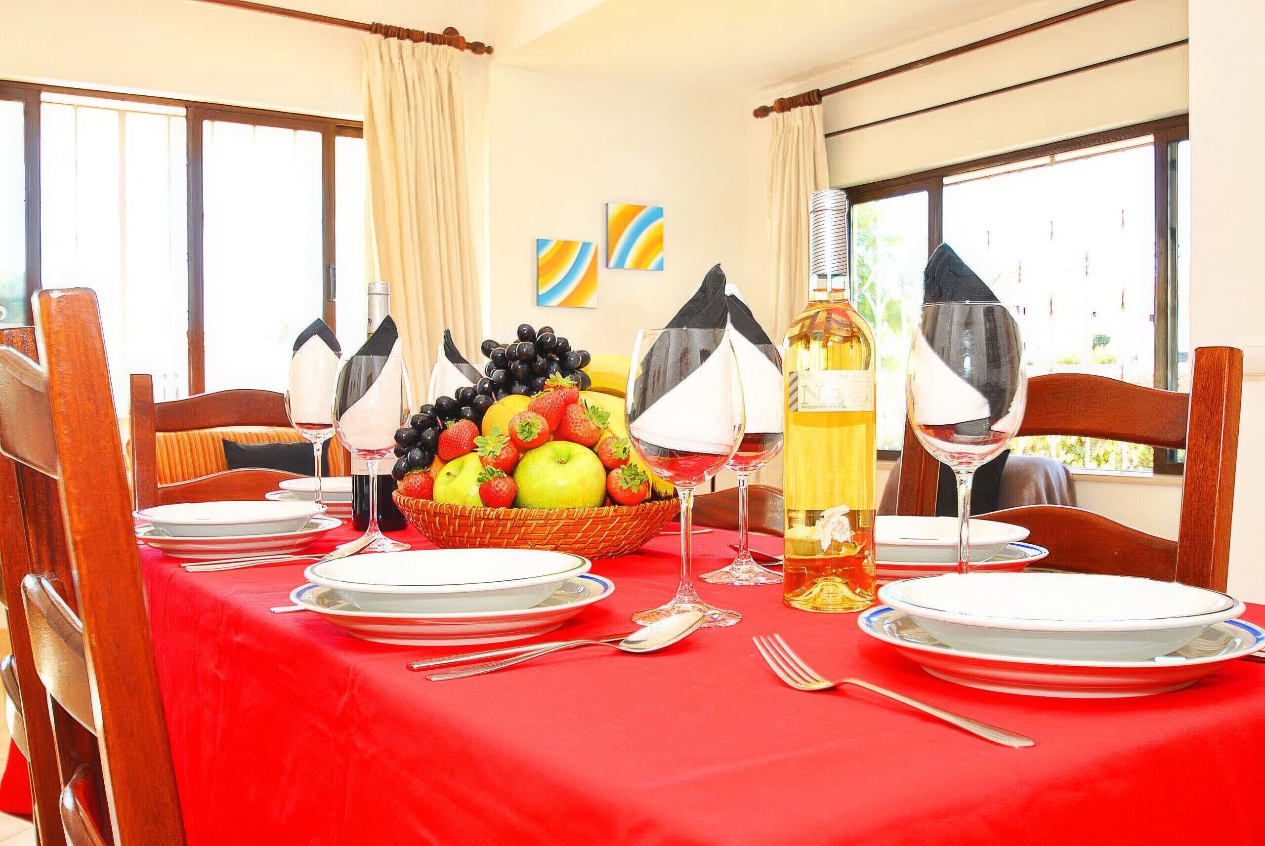 A dining table set with plates, cutlery, glasses, a fruit basket, and a bottle of wine.