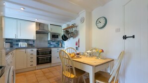Een keuken met witte kastjes, een magnetron, een oven, en een houten eettafel met stoelen.