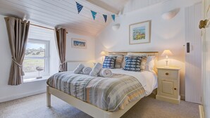 Een slaapkamer met een bed, nachtkastjes, een raam, gordijnen en decoratie aan de muur.