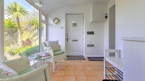 Een lichte kamer met een groot raam, rieten meubels, een witte deur en een klein tafeltje met kop en schotel.