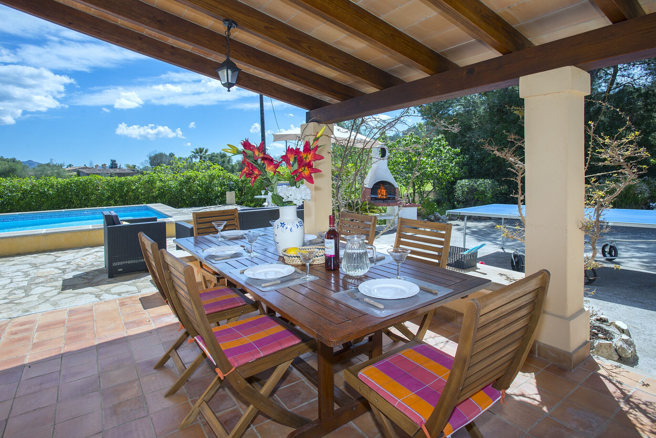 An outdoor patio with a wooden table set for dining, surrounded by chairs with colorful cushions.