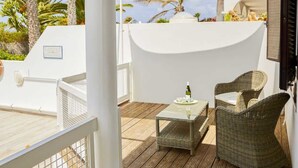A balcony with wicker furniture, a glass table, and a bottle of wine.