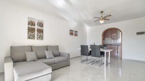 Ein modernes Wohnzimmer mit einem grauen Sofa, einem Esstisch mit Stühlen und einer durch einen Bogen sichtbaren Küche.