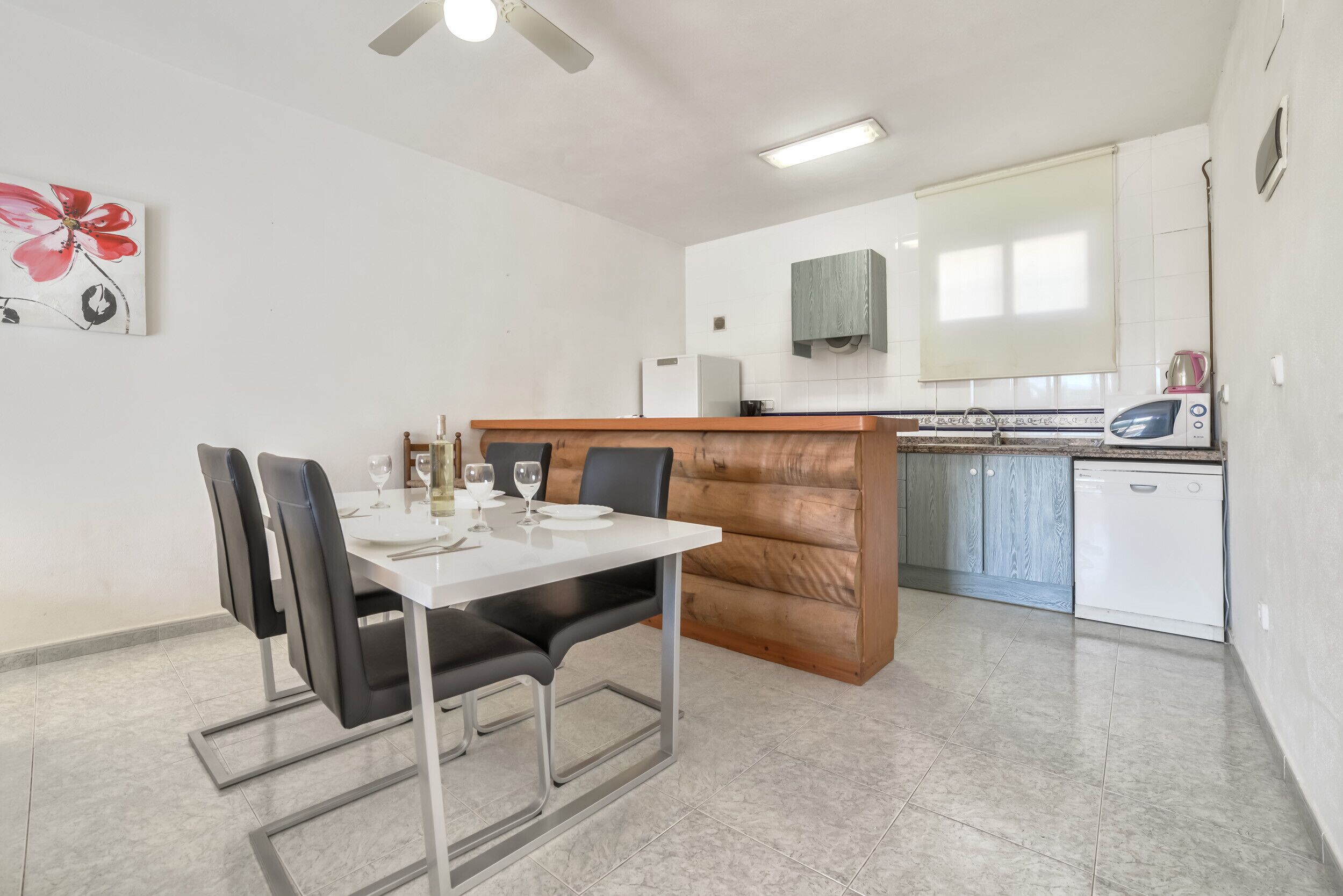 A modern kitchen with white cabinets, a wooden countertop, and a dining area with a white table and black chairs.