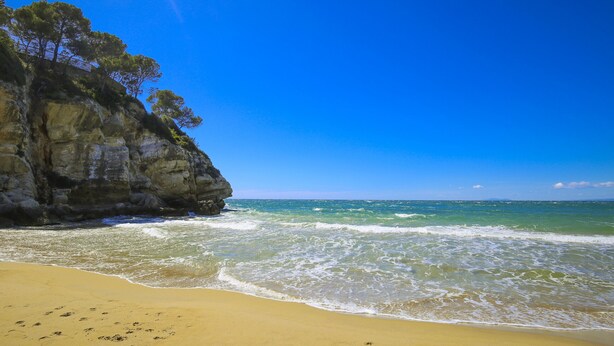 A beach with clear blue water, sandy shore, and rocky cliffs. - Private swimming pool and jacuzzi in Cap Salou (Salou)