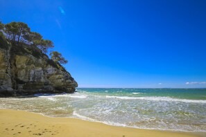 A beach with clear blue water, sandy shore, and rocky cliffs.