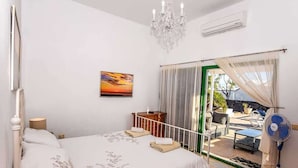 Ein Schlafzimmer mit Bett, Nachttisch, einer Deckenleuchte, einer Wand-Klimaanlage, einem Fenster mit Vorhängen und Blick ins Freie.
