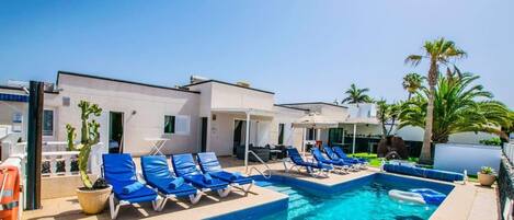 A swimming pool with lounge chairs, a lifeguard stand, and palm trees.