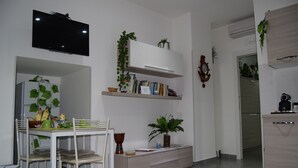 A modern kitchen with a dining area, white cabinetry, a flat-screen TV, and decorative plants. - Detached apartment (Salerno)