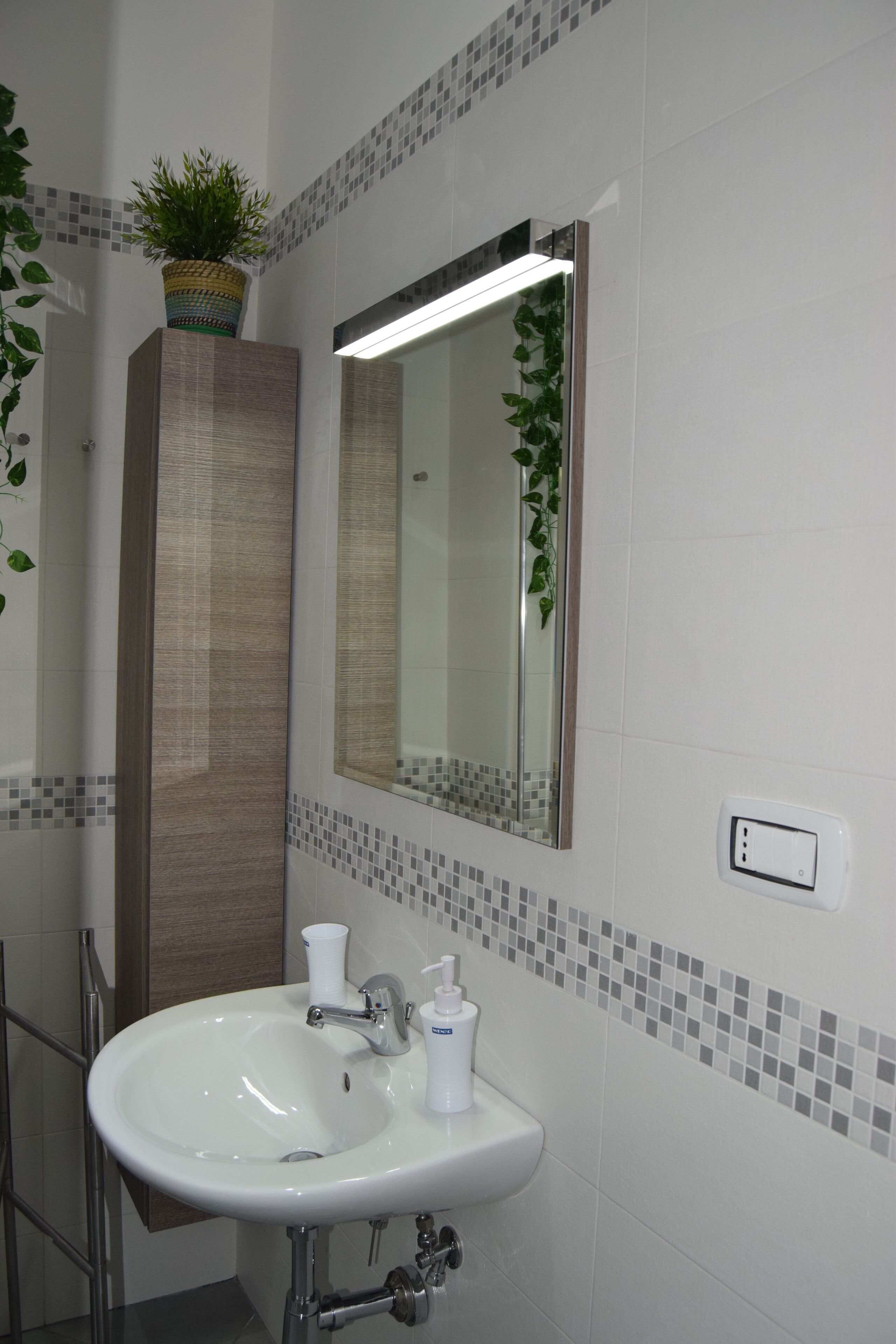 A bathroom with a white sink, a mirror, a potted plant, and a tiled backsplash.