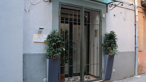 A building entrance with a metal gate, two potted plants, and a sign above the door. - Detached apartment (Salerno)