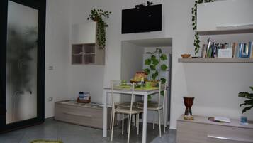 Un salon moderne comprenant une table à manger, des chaises, un téléviseur, une bibliothèque et une plante.
