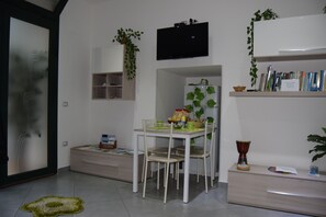 Ein modernes Wohnzimmer mit Esstisch, Stühlen, Fernseher, Bücherregal und einer Pflanze.