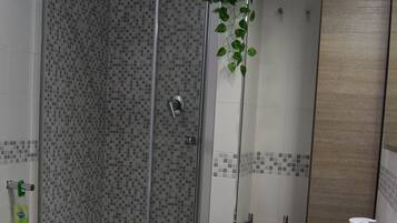 A bathroom with a shower, bidet, sink, and a potted plant.
