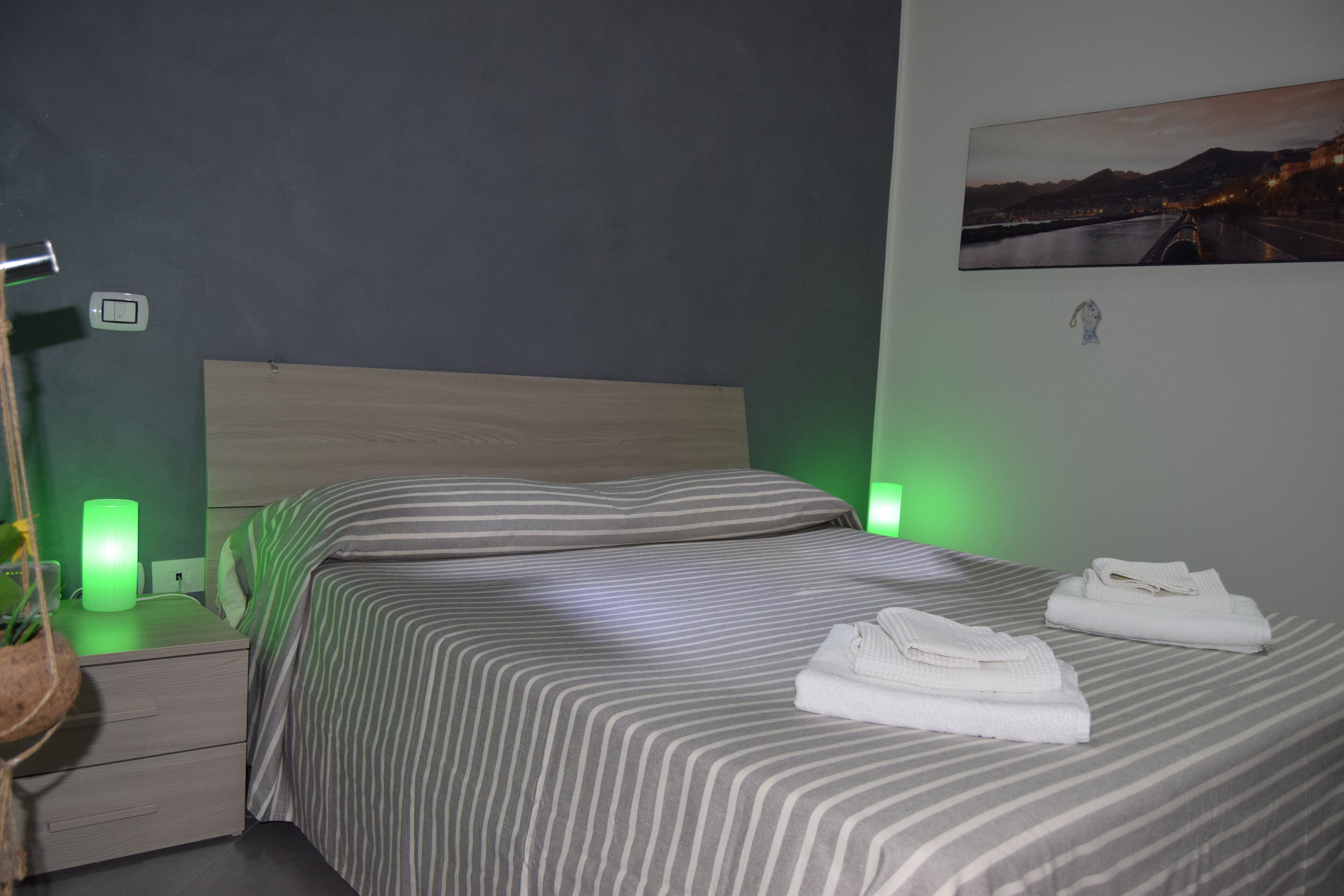 Una camera d'albergo con un letto, abat-jour, comodino e un quadro appeso al muro.