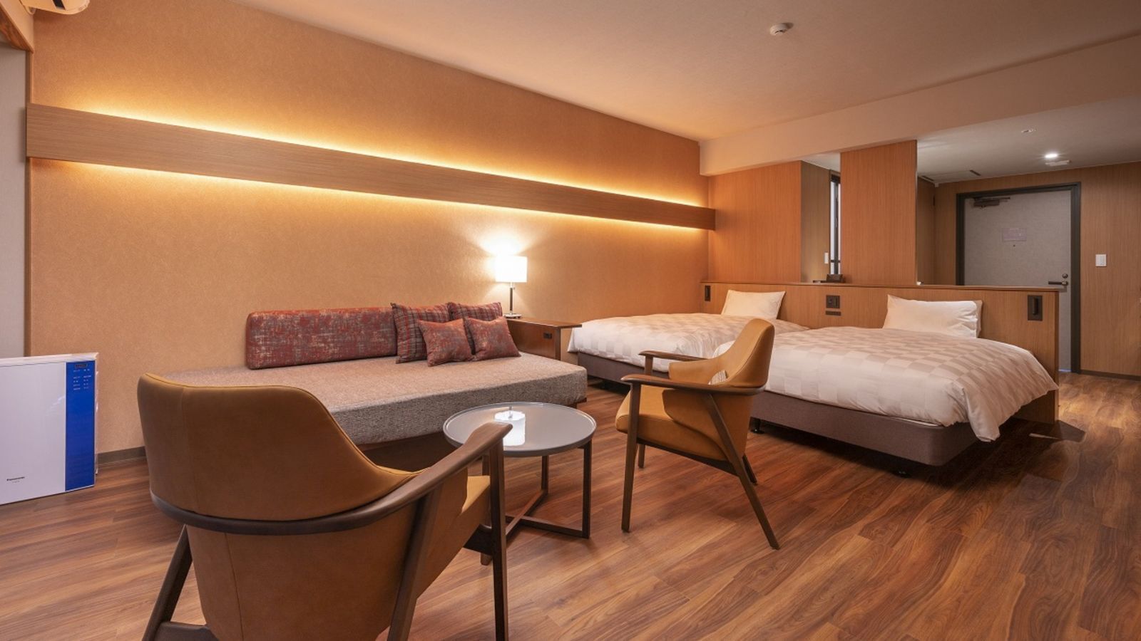 Una habitación de hotel con un sofá, dos camas individuales, una mesita y una silla.