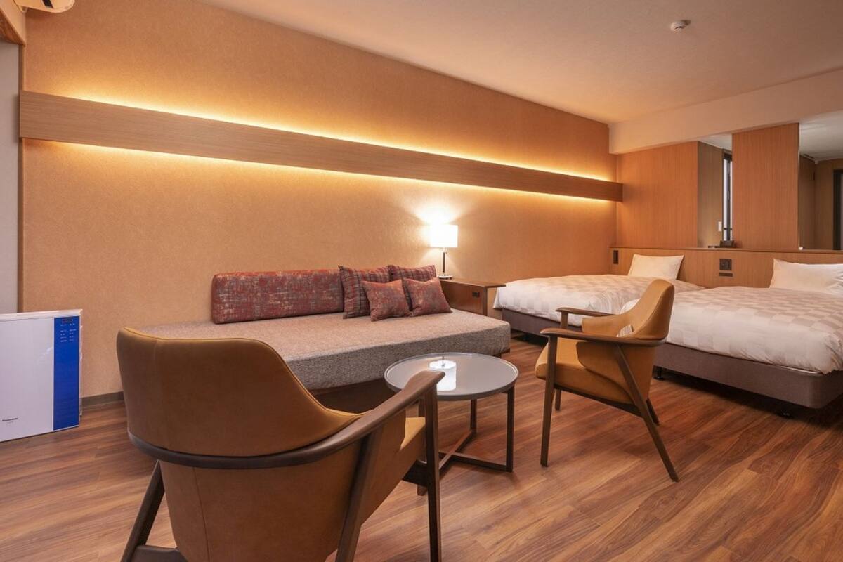 Una habitación de hotel con un sofá, dos camas individuales, una mesita y una silla.