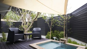Een terras met een jacuzzi, twee rieten stoelen en een tafel onder een luifel.