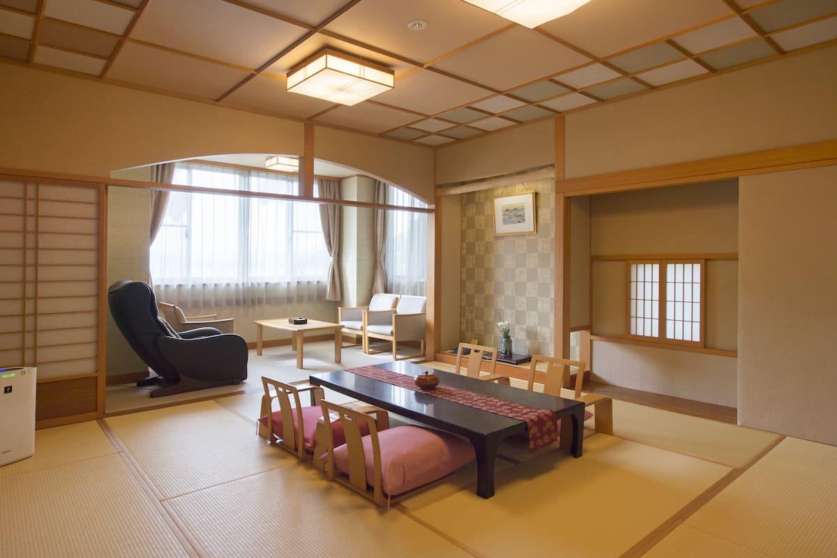 Una habitación tradicional japonesa con suelo de tatami, una mesa baja, sillas y una cama futón.